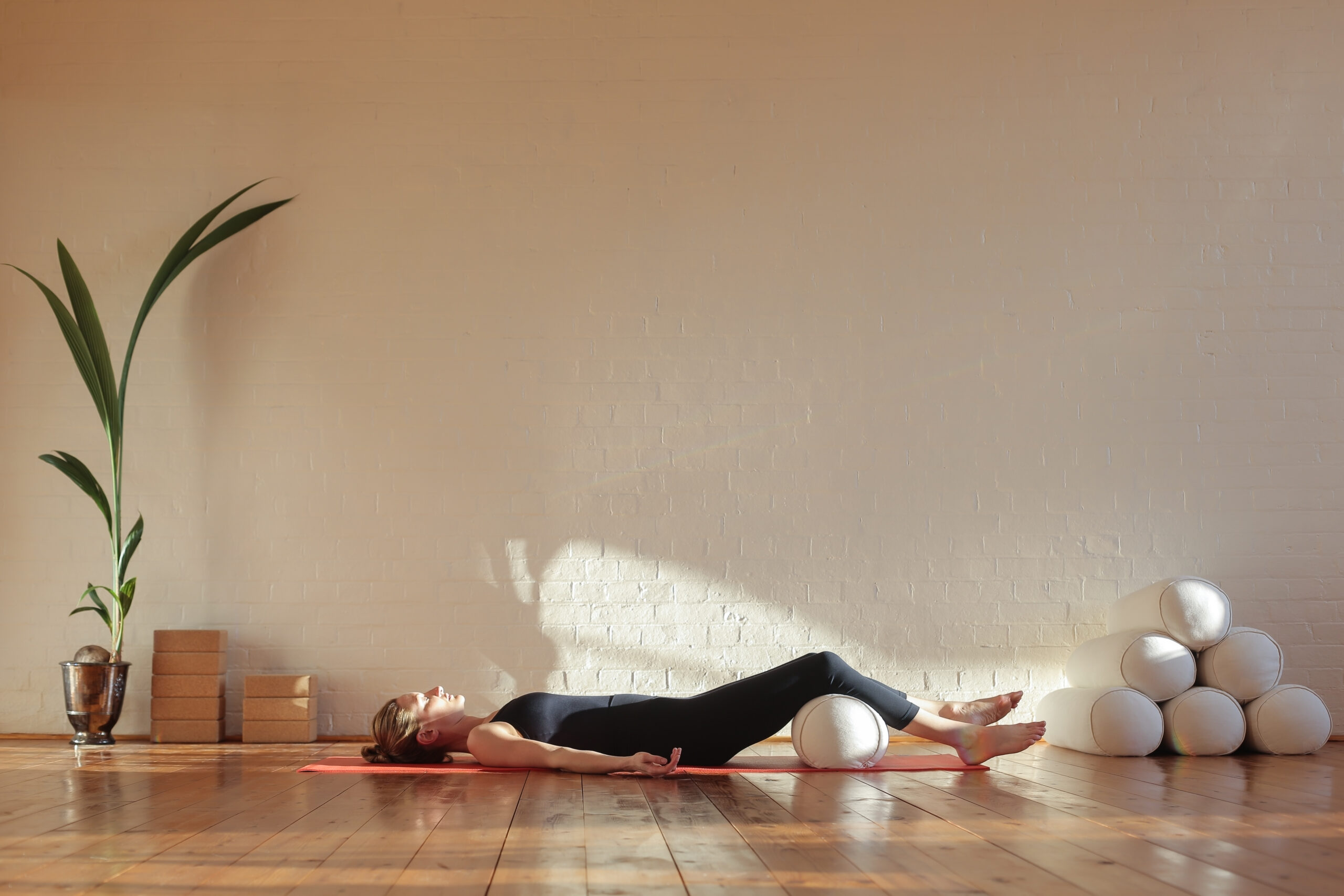 Young,Woman,In,Corpse,Pose,With,Knees,Resting,On,Bolster